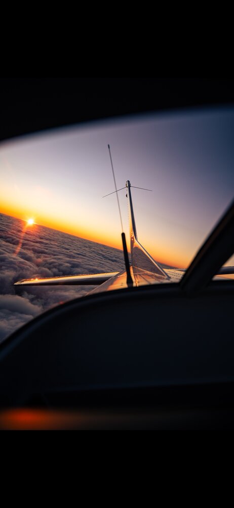 Aircraft tail and wing silhouetted against a sunset horizon