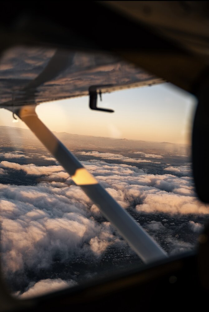 View past the wing over clouds at sunset with mountains in the distance